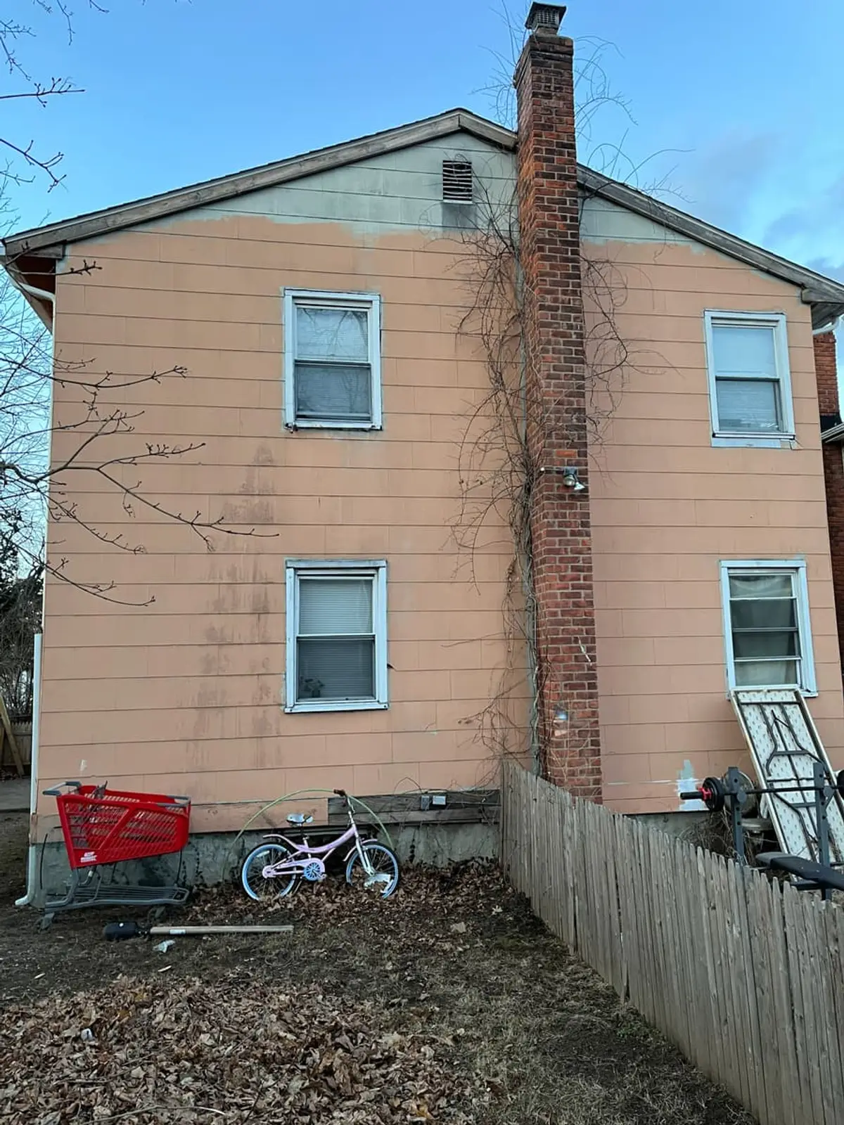 Selling a condemned house in Hempstead: back of a two-story house with a brick chimney and a leaf-covered yard