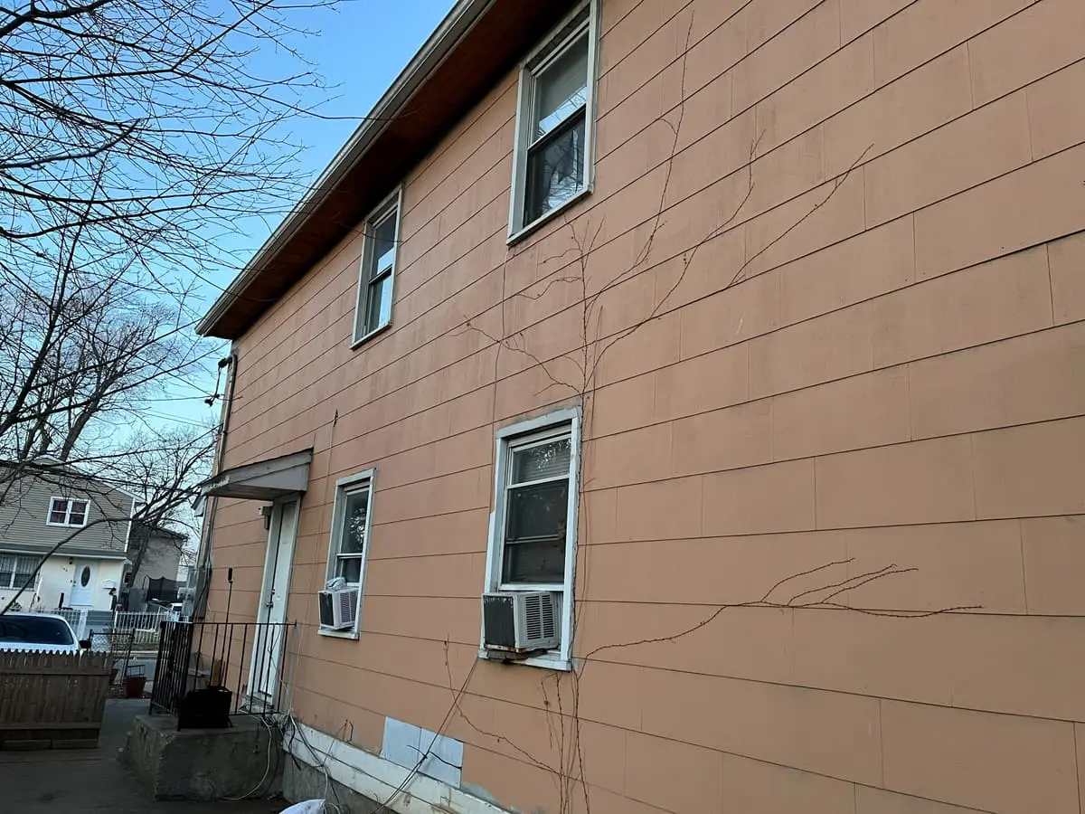 Selling a house as-is in Hempstead: two-story house with faded, cracked siding along the side